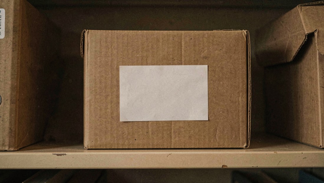 Gesloten archiefdoos met een label op een plank, in gedempt licht, zonder enige leesbare naam op het label